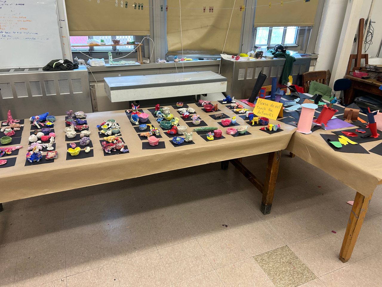 Dozens of small student-made clay sculptures lined up to dry on a paper-covered table in a TNS classroom