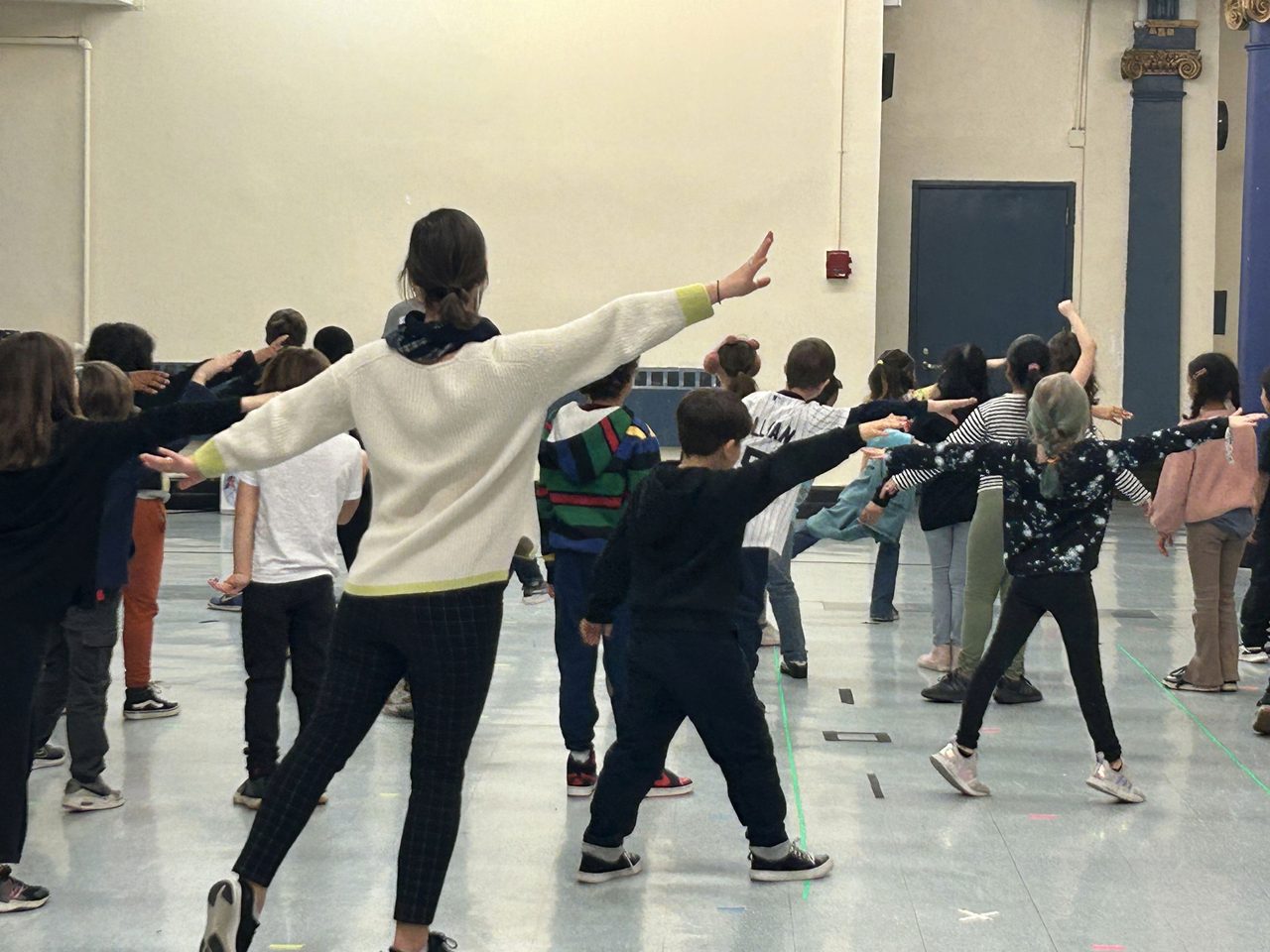 TNS students stretching their arms wide during a movement and dance class in the school auditorium