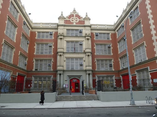 The Neighborhood School exterior — a four-story red brick schoolhouse with large windows and bright red doors, located in NYC's East Village