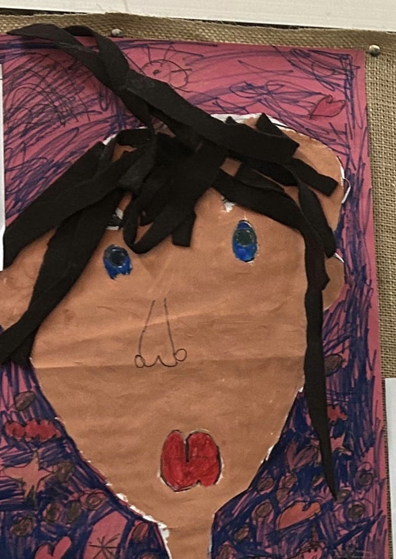 A kindergartener's mixed-media self-portrait, painted and collaged with yarn hair, on display in a TNS classroom